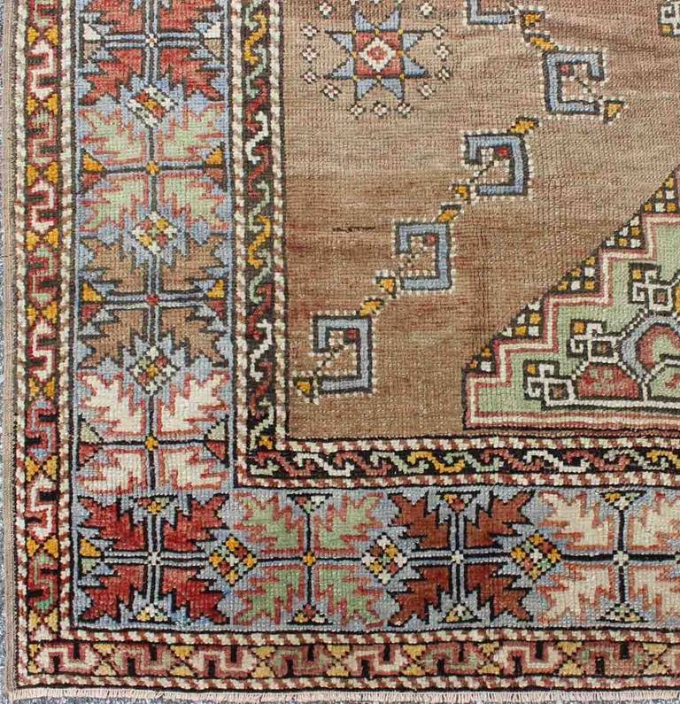 Turkish Oushak Carpet in Light Brown, Light Blue, Light Green, Taupe and Red.
Set on a camel/light brown  background with a gray-blue border, this unique medallion Oushak displays a colorful, yet subtle, color combination. 
Measures: 5'7 x 8'0.