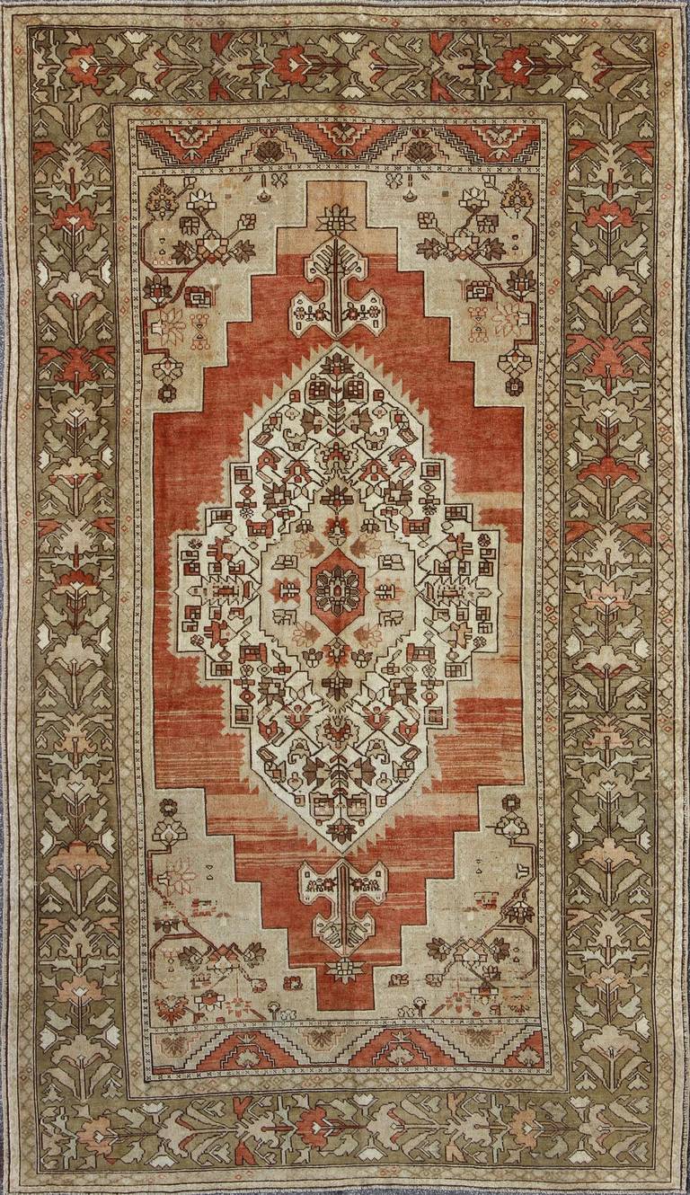 This beautiful Turkish Oushak rug, handwoven in Turkey, beautifully integrates neutral compositions and features an exquisite geometric design with a large central medallion. The wide border of taupe and green surrounds the multi-color background of