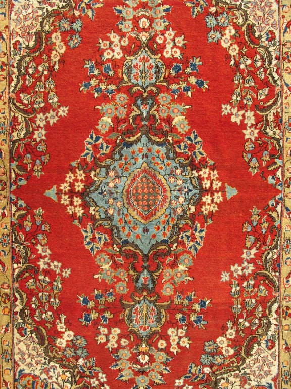 This beautiful vintage Persian Qum rug bears a stretched central Medallion of blue with an impressive array of flora surrounding its body. The red field plays host to a delightful display of winding flowers that press upon the organically formed