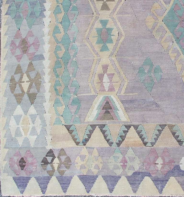 Large Vintage Kilim in Light Purple, Lavender, Turquoise, Gray & Butter Yellow.
This unique and stunning Turkish Kilim dates back to the 1950s. With a purple-gray background and blue-gray lavender medallions and corners, its bold and geometric