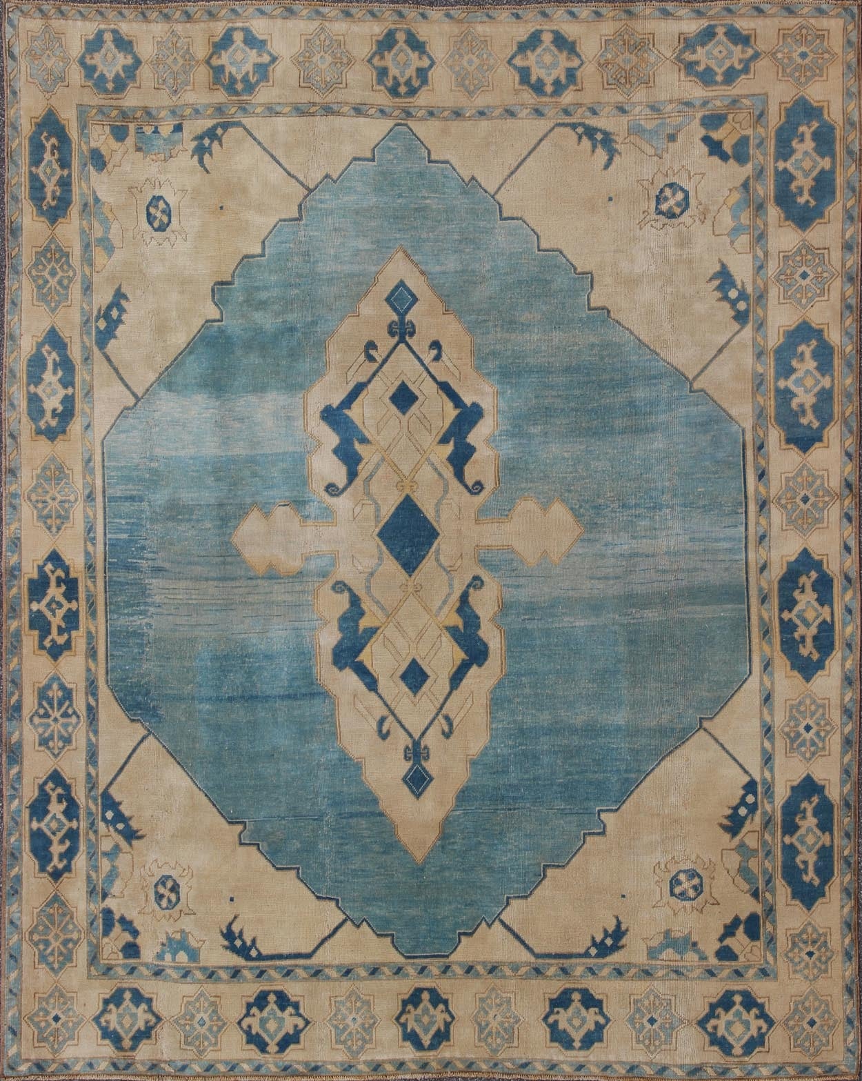 The large-scale design of this mid-20th century Turkish piece showcases a large medallion framed by a sky-blue background and a border of delicate turtle motifs. Soft ivory and cream hues highlight the tribal pattern. Renowned for their distinctive