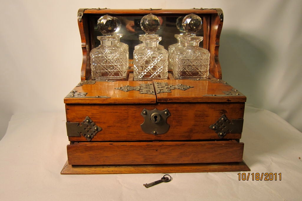 This early twentieth century English oak designed tantalus is accented with nickel plated bronze decorated hardware. The unit contains three superb patterned cut glass decanters, each placed in its own 
