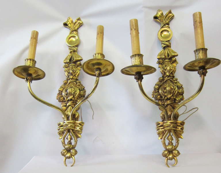 A vintage set of four (4) stunning wall sconces. They are French & from the early 20th century. The sconces are sculpted in dore' bronze. Each features an elongated decorative wall plate & two (2) candelabra arms extending out from the center of