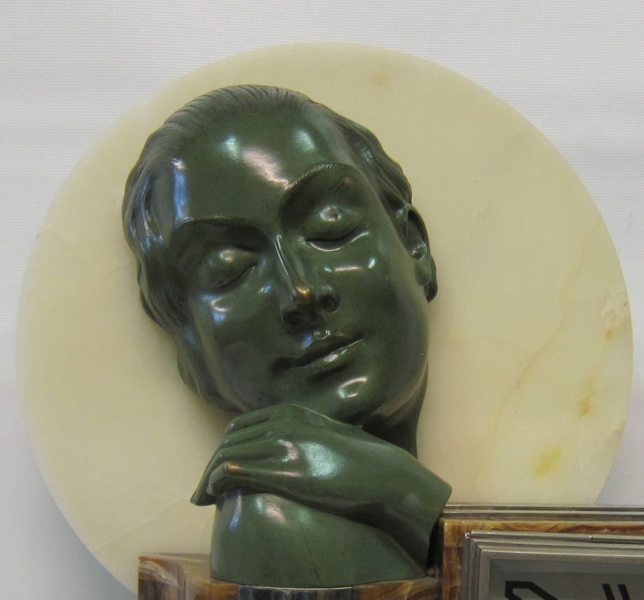 A beautifully sculpted Art Deco clock featuring a bronze bust of a woman. This bust, with an age defining rich green patina, sits atop a classic period geometric designed base of marble and onyx and is further highlighted by a circular white marble