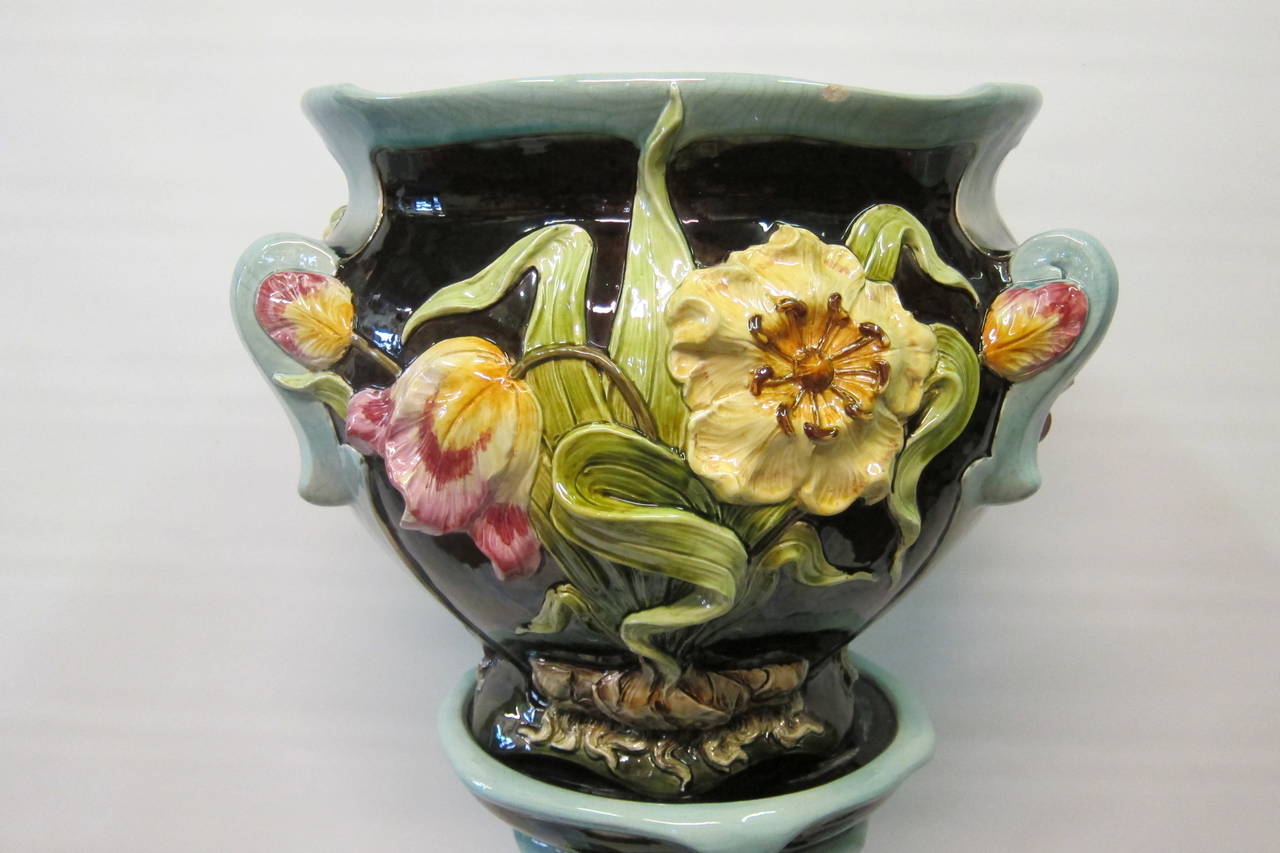 This unique Continental Art Nouveau jardinière & pedestal dates from the early 20th century. It is decorated with a vivid array of colorful sculptured flowers against a cobalt blue background with light blue accents. The unit is made of pottery