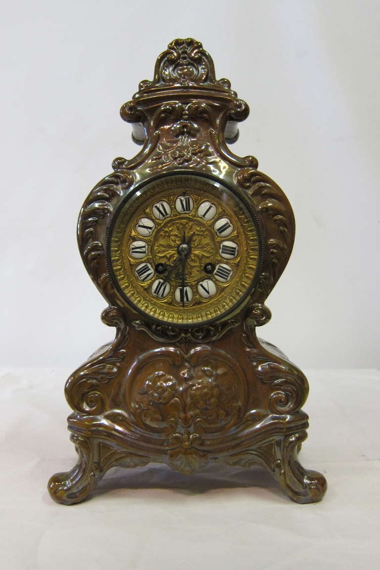 An unusual French Faience mantle clock designed in a rich earthy lustrous tin glaze over a molded pottery body. Circa late 1880's, the body of this footed timepiece is decorated with flowers & scrolls within its design.
The clock has the original
