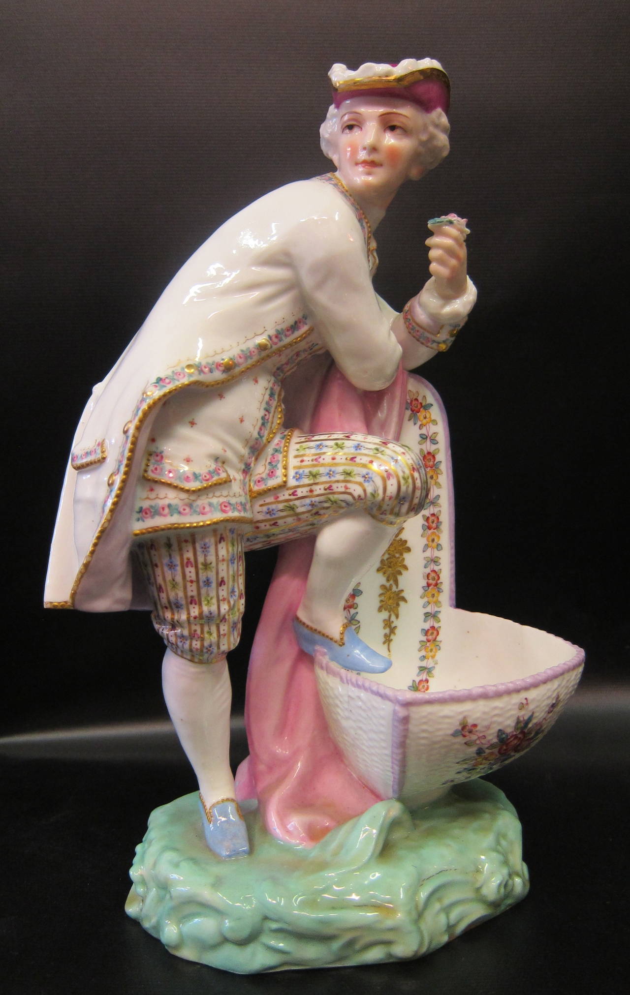 This rare & vintage pair of porcelain table salts features colorfully costumed figures of the country gentry. Each statue is sculpted & detailed with such precision that bespeaks a standard of high quality. Each figure is posed beside a huge master