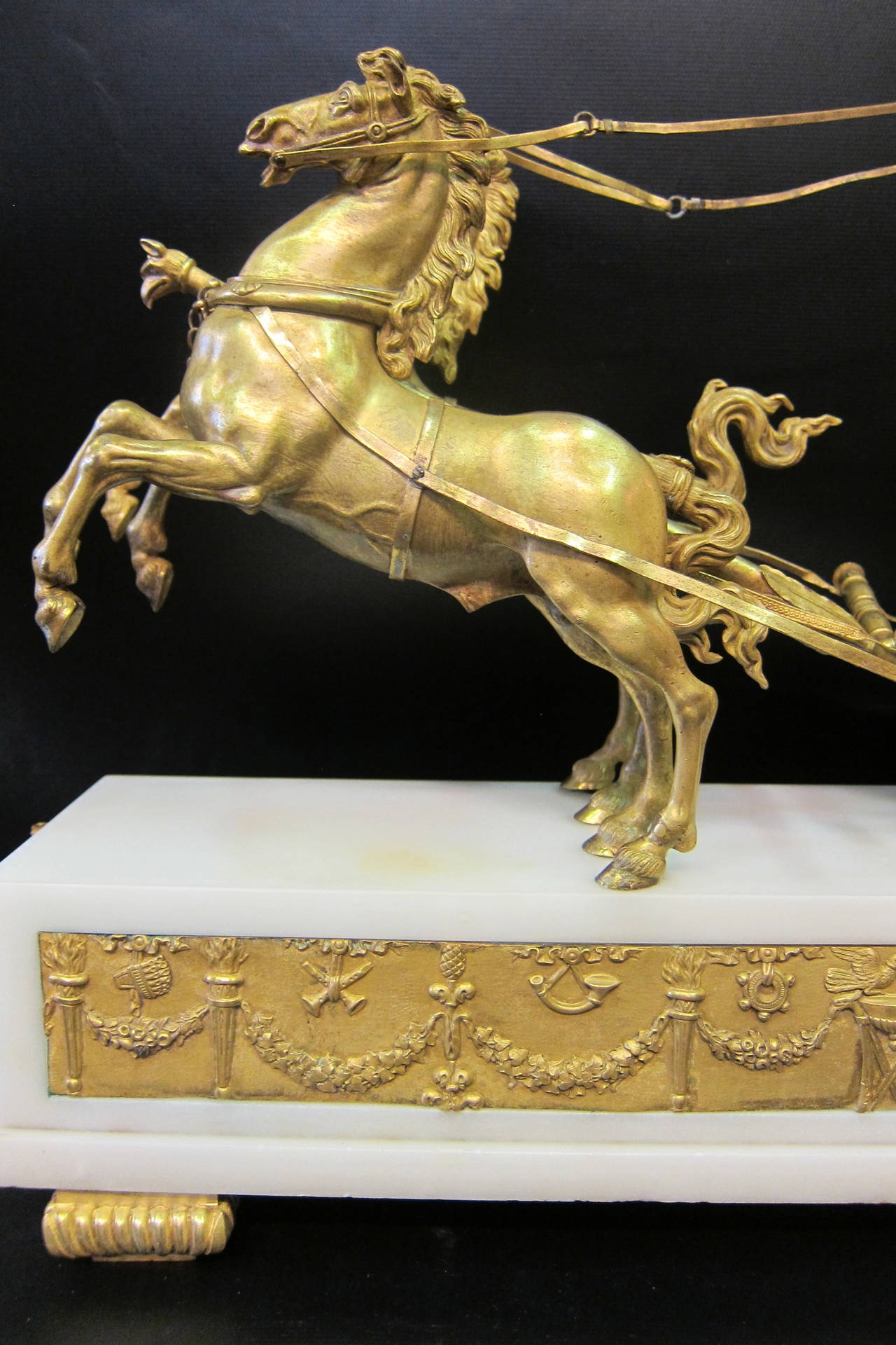 This vintage, circa 1855, French Empire mantle clock is designed with a core' bronze mythological subject mounted upon a footed white marble platform. The  mounted bronze sculpture is that of the goddess Aurora, racing against time to chase the