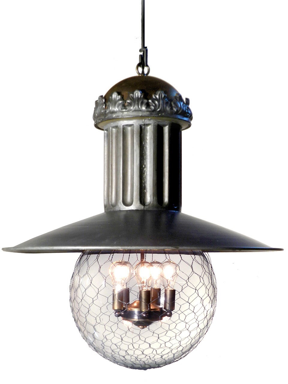 This oversized and highly detailed lamp features a fluted column, pressed floral tin crown and copper dome. It's illuminated with a five bulb cluster and surrounded by a 14 inch globe covered with a protective wire mesh. The dark patina and
