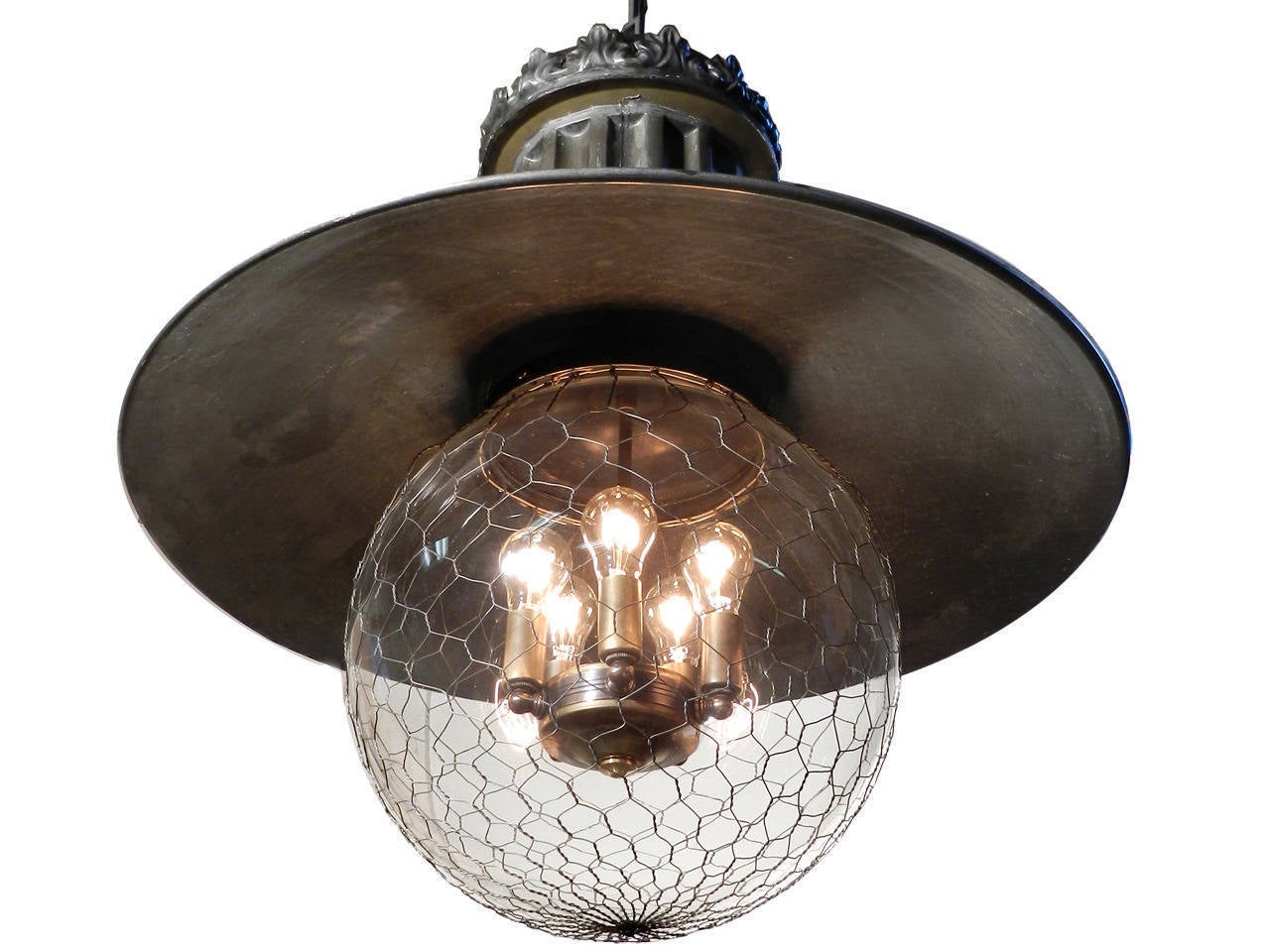 This oversized and highly detailed lamp features a fluted column, pressed floral tin crown and copper dome. It's illuminated with a five bulb cluster and surrounded by a 14 inch globe covered with a protective wire mesh. The dark patina and