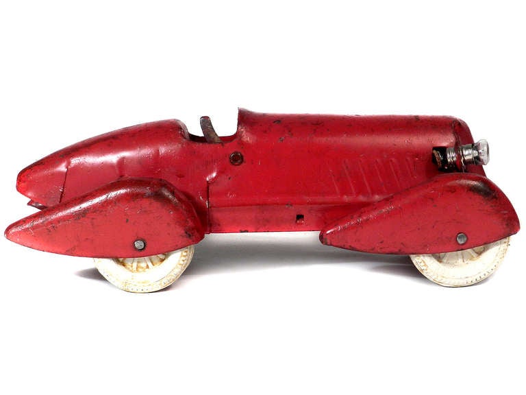 This is a real stylish boat tail toy race car with futuristic-looking fender skirts and white rubber tires. It was made by the Wyandotte toy company in the 1930s. It has almost all the original red paint and shows some wear. This one has just the