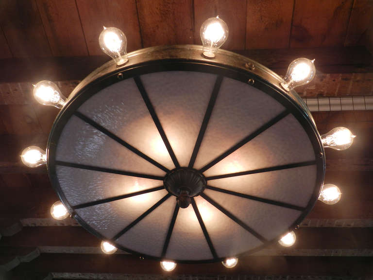 This is an impressive theater lobby chandelier. inside are four bulbs to light the flat  opaline glass wheel. The outside ring has 12 exposed bulbs with a total diameter of over 3 feet. It has a striking look with clean simple lines. Everything on