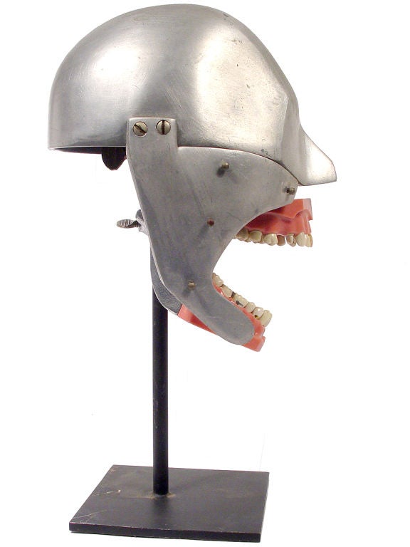 This is a teaching and practice device used by dental school students. It's life sized and was a stand in for the real patient. The machine-age looking polished aluminum head sits on a custom made iron display stand. This beautiful example has the