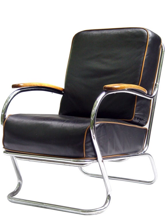 This is an authentic 1950's chromed tubular steel streamlined chair. It's very heavy cushions are covered in a soft black glove leather with contrasting camel colored piping. The piping complements the natural finished wood arms. The leather is in