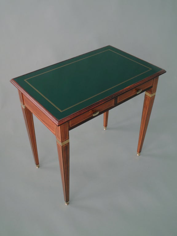 A two-drawer rosewood side table with brass fittings. The lacquered glass top with gilt detail. After a design of Paolo Buffa.