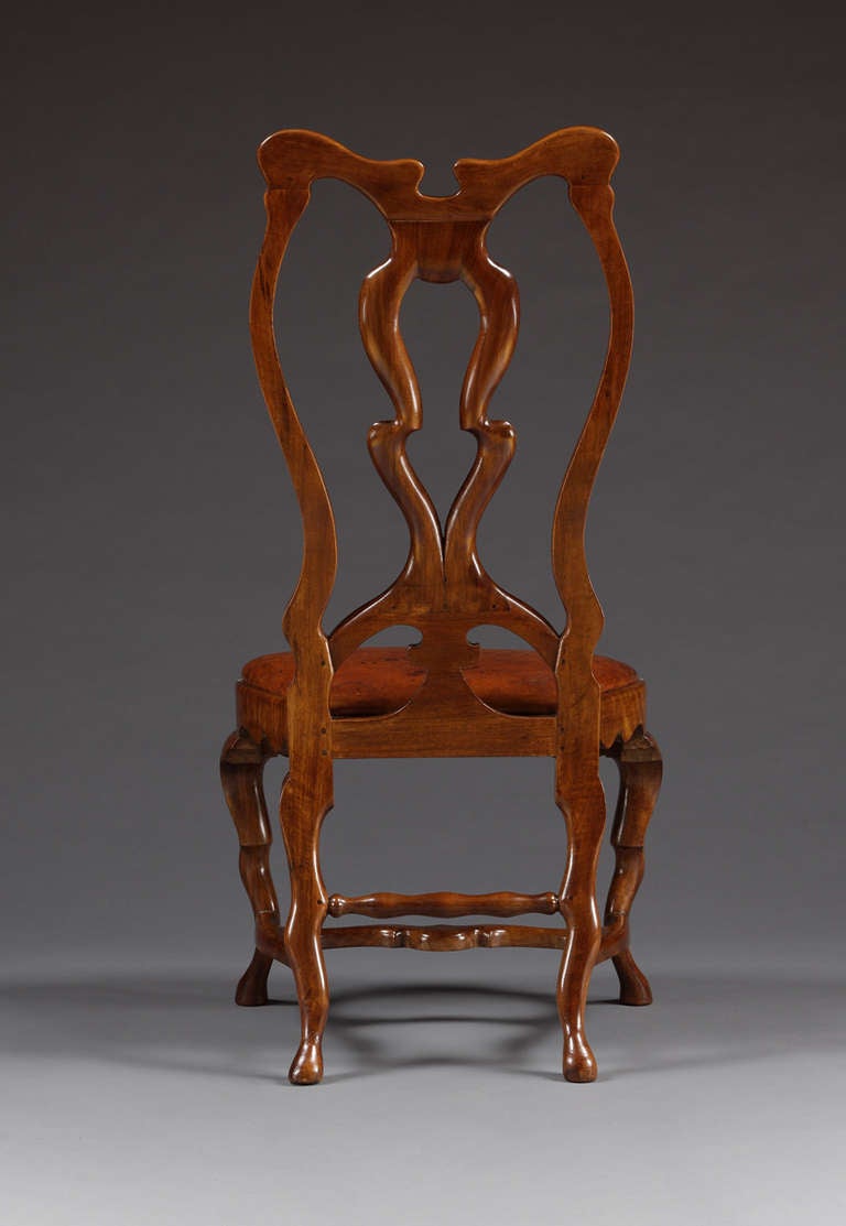 Each chair with foliate carved top rail supported by a shaped and pierced central splat, flanked by profoundly curved uprights.  The whole back resting on an arched section with central carved support.  The lobed and serpentine seat rail with shaped