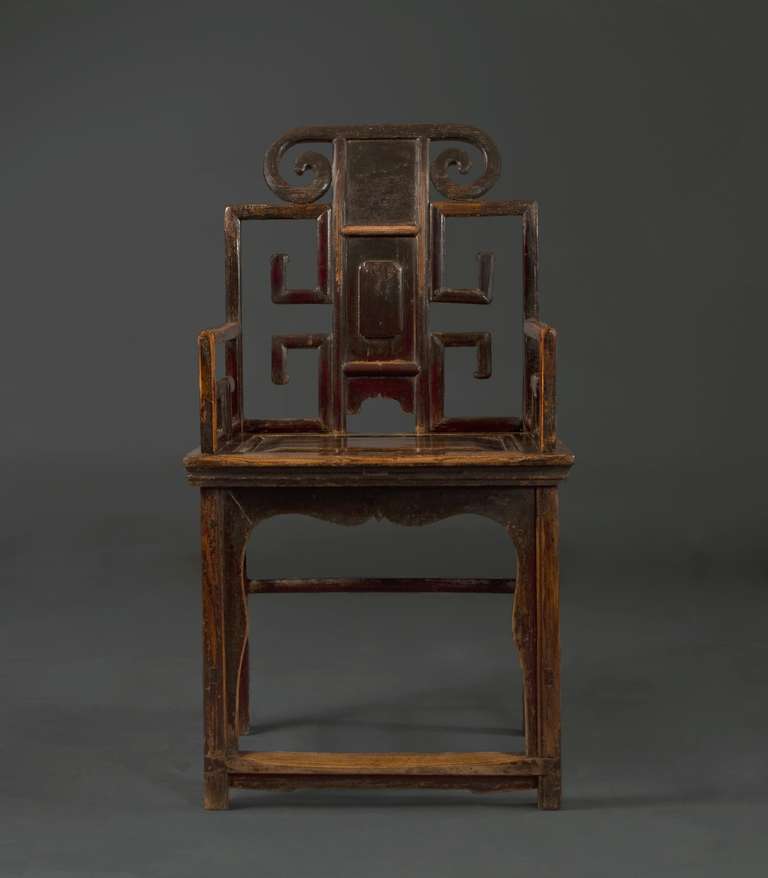 The top rail carved with scroll ends above a rectangular back splat inset with a rectangular panel flanked by openwork archaistic angular scrolls continuing to the similarly carved arms. The seat with a molded edge supported on four straight legs