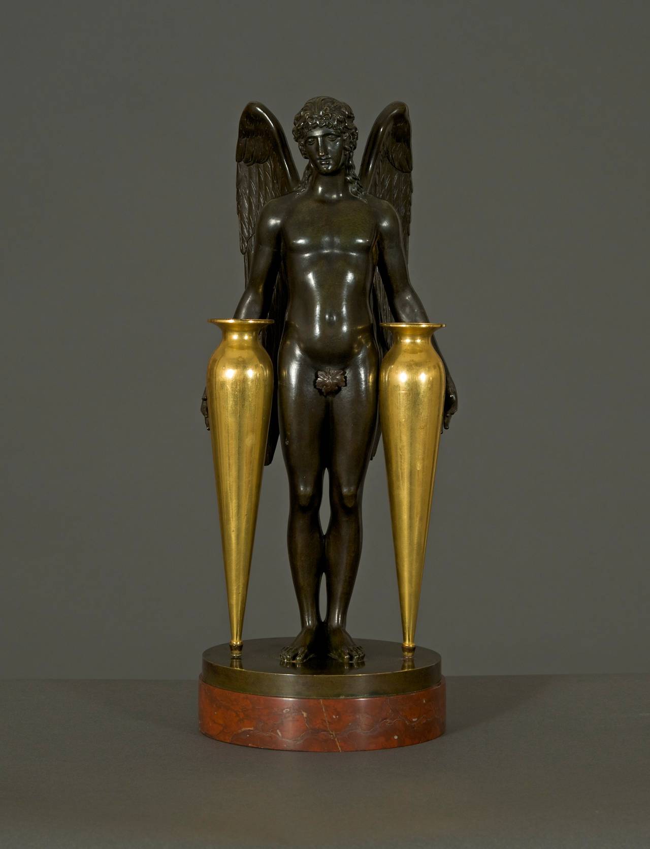 Of winged male form holding two elongated gilt-bronze handleless amphorae raised on a circular base of Rouge Griotte. Detailed research report available on request.