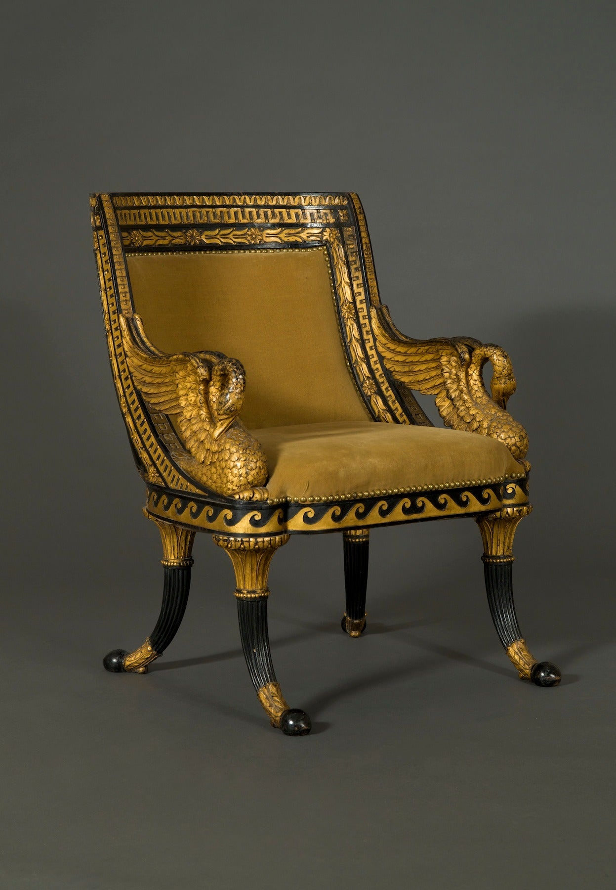 The curved upholstered backrest bordered by rows of waterleaf, greek key and laurel leaf carved and gilt ornament, and completely ebonized to the back The upholsdered seat flanked by gilt armrests carved in the form of swans above an ebonized seat
