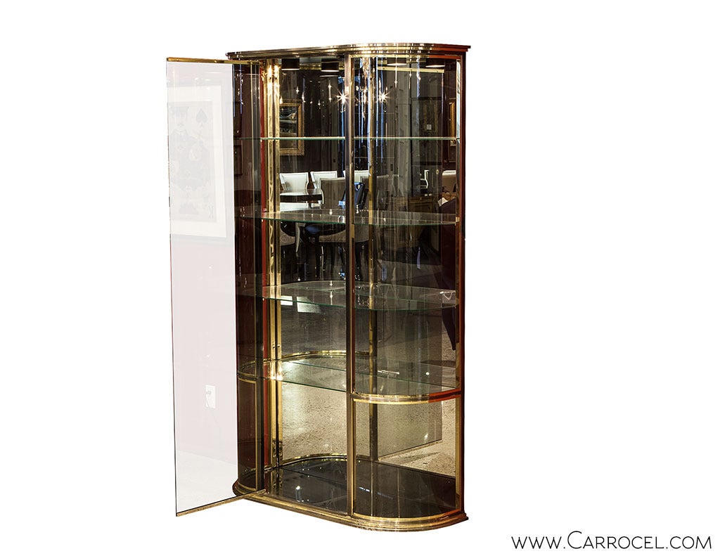 Unique demilune shaped glass front vitrine. Solid brushed chrome moldings around top, bottom and down each side of the central front door, accented by brass trim. Internal lighting that shines through four floating glass shelves.
