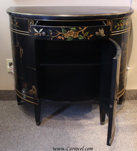 This is a commode made by the renowned Imperial Furniture of Grand Rapids, Michigan in the 1940s. It is done in a sleek ebony finish with beautifully detailed hand-painted imagery of an outdoor Oriental scene. Its demi-lune shape allows you to place