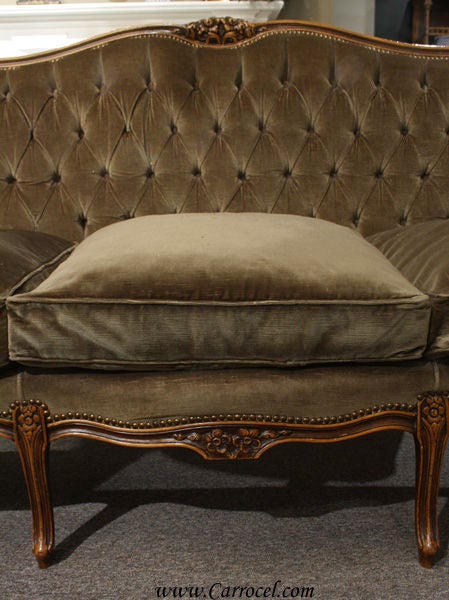 This lovely sofa is an antique from America. Made in the 1930s, it is modeled after the French Louis XV style of furniture. It features beautiful Louis XV hand-carvings and is solid walnut. The upholstery is a rich dark green velvet fabric with