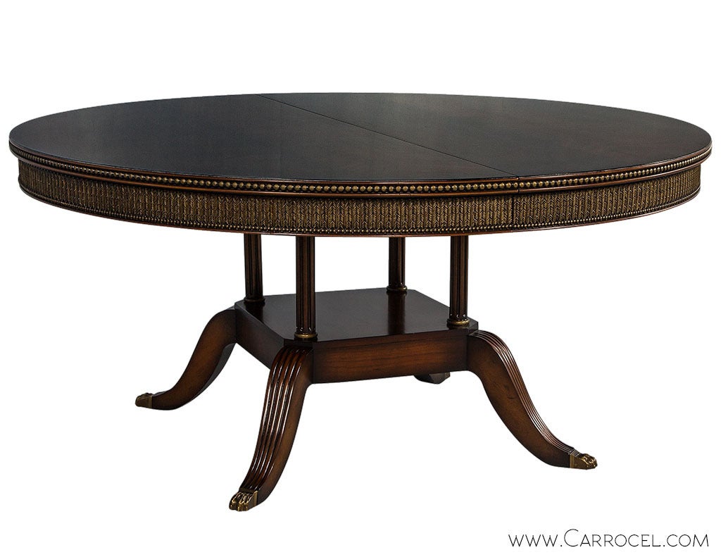 Custom flamed and feathered round mahogany formal dining table with birdcage pedestal base. Beautifully finished with a hand rubbed patina and hand painted antique gold accents on the beaded edge, feathered acanthus apron and pedestal rings. This