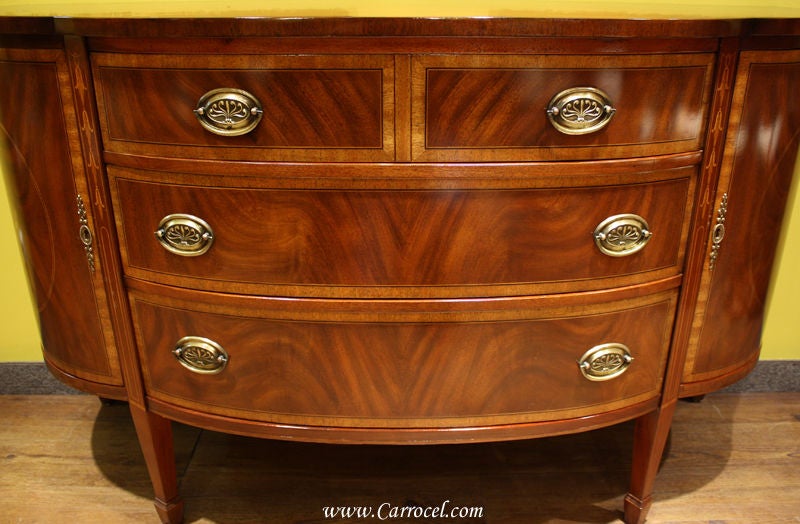 This federal style demi-lune sideboard is an antique piece that has been professionally refinished by our master artisans here at Carrocel Restorations. Made in the 1930s, it features solid mahogany construction with flamed mahogany and light