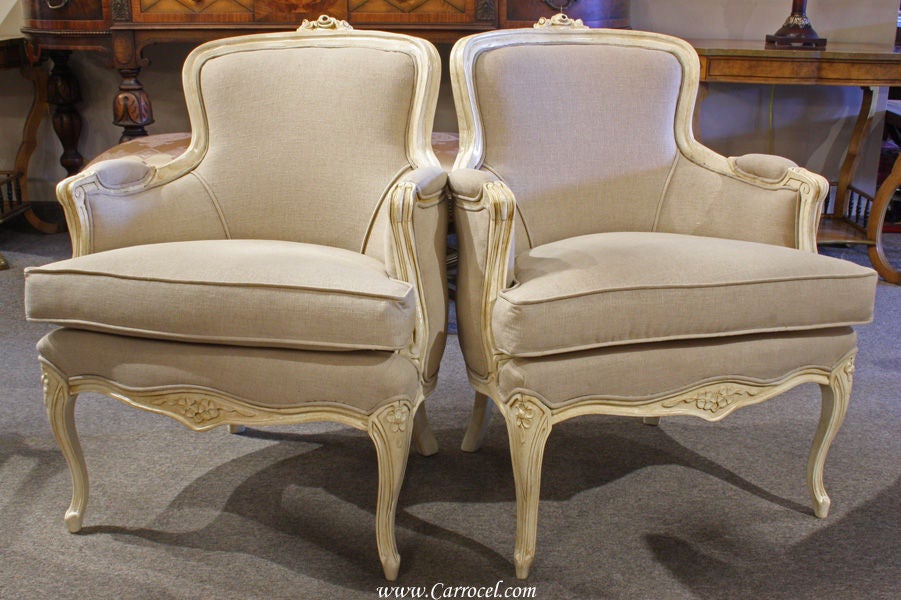 This is a pair of antique solid wood living room chairs. Made in the 1930s and modeled after the delicate Louis XV style, these chairs have been professionally upholstered by our skilled artisans. Painted in a soft cream white finish that lends