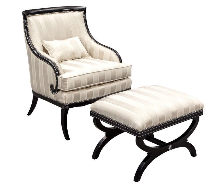 Pair of Hollywood Regency parlor lounge chairs with ottomans. Black lacquered, hand polished with silver accents.