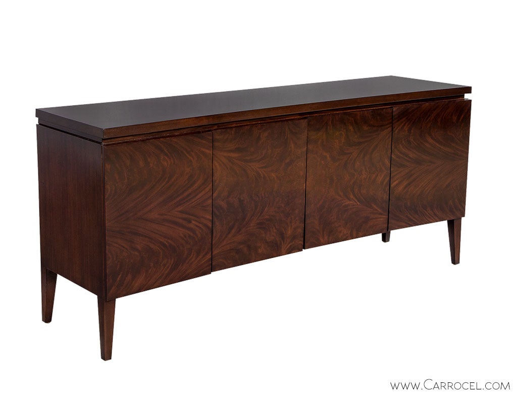 Stunning Transitional styled four door sideboard buffet in ribbon mahogany with a book matched sunburst pattern across the front. Clean flowing lines with a gentle concave design on raised tapered mahogany legs complement this elegant piece. Suited