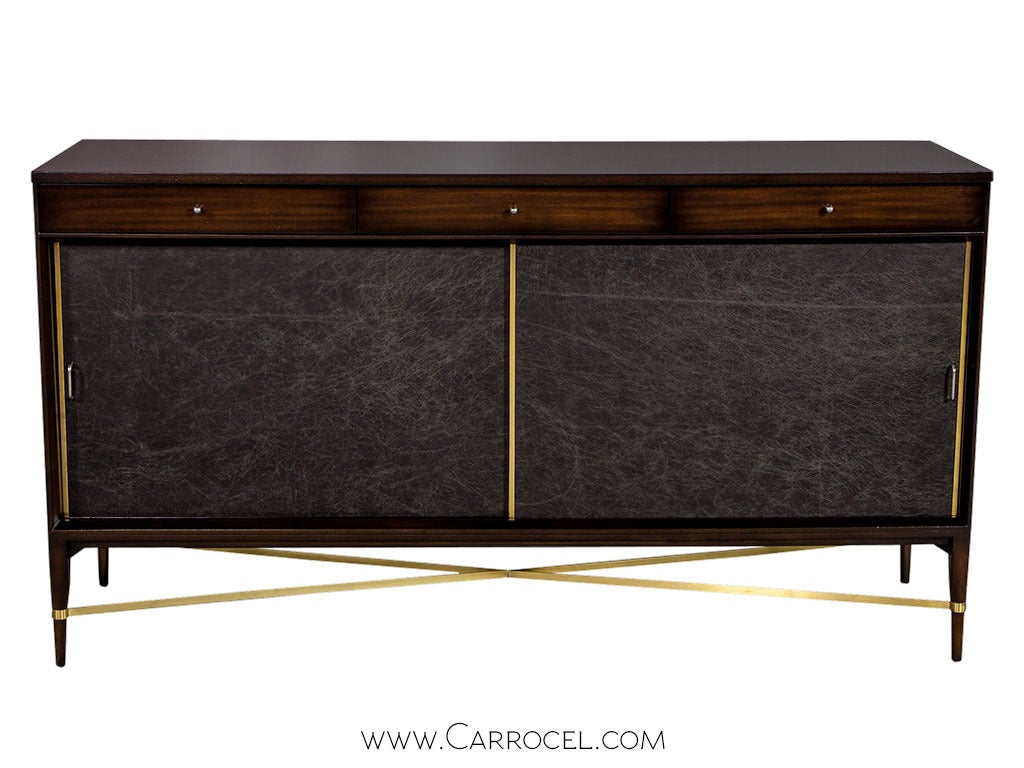 A classic Mid Century Paul McCobb piece, complete with the richness of mahogany, the elegance of tapered legs, in a simplistic geometric style, newly restored by Carrocel craftsmen with accent brass edgings and leather fascia. This credenza, an