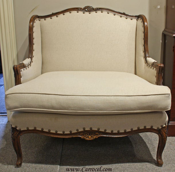This lovely bergere French Country chair is made in the 1950s and is solid walnut.  It has been professionally restored by our master artisans and craftsmen in a soft 100% linen fabric.  It has been finished with large antiqued upholstery nails for
