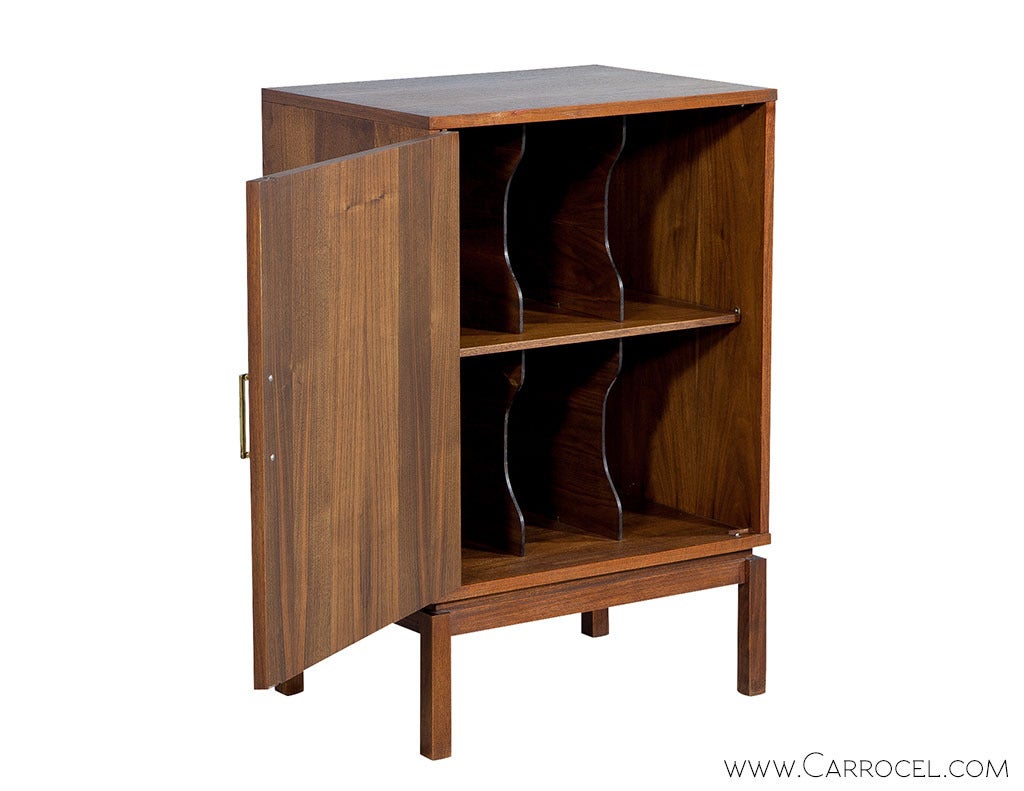 A teak wood classic with an authentic Mid Century Modern design. The cabinet stands on simple teak posts, with the interior divided into multiple compartments. The exterior showcases the original finish, original brass hardware and a door front