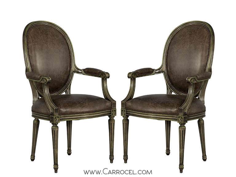 Leather antique louis XVI parlor arm chairs recently refinished and reupholstered by our craftsmen in a distressed brown leather and finished in a distressed leaf verd finish.