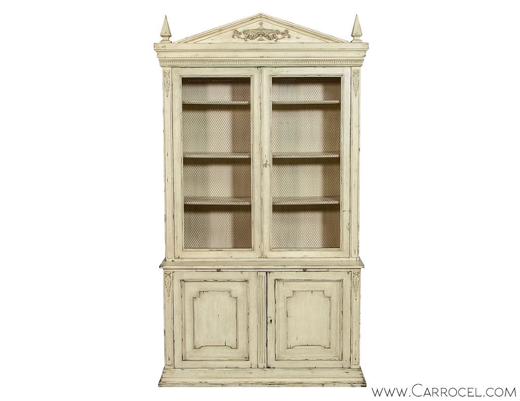 Built in two parts, this vintage display cabinet combines visible and closed shelving in the rich geometrical elegance of the Neoclassical style. The upper unit, with shelves covered by framed bird cage doors, and a pediment flanked by pyramid