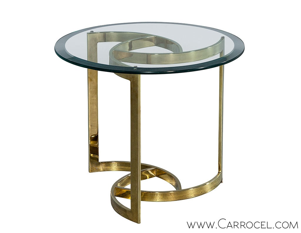 Stunning vintage polished brass end table with a three-arm pinwheel design. Thick, round, beveled edge glass tops the stunning base.  A gorgeous piece in excellent original condition. This table will bring elegance and taste to a space.