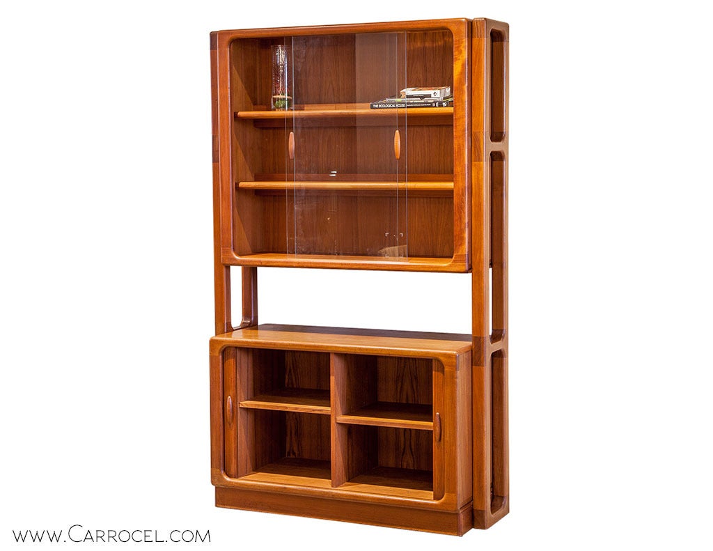 A Mid Century display cabinet in excellent condition, fashioned in natural teak with lightly filleted edges and subtle variations in color that enhance its classic appeal. Tamboured bottom doors and sliding glass panels in the upper section overlay