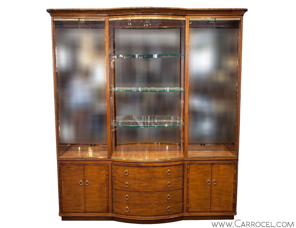 A spacious breakfront display cabinet from Drexel's Heritage Collection, in a warm walnut palette, with a curved projected central bay of four lower drawers and a bowed glass front, flanked by cabinets on either side. The beauty of this piece lies