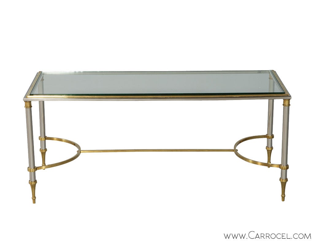 Bring home some Hollywood Regency glamour with this brass and steel cocktail table in the style of Maison Jansen. Four steel posts with truncated sphere sections feature knees and spade feet in brass and support a clear glass top. Brass also accents