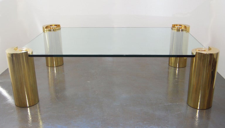 Karl Springer coffee table with glass top on four polished brass columnar legs, with heavy brass plates and caps. Legs 8