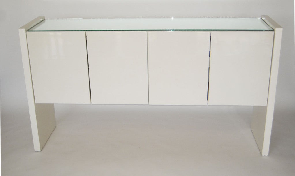 Superb minimalist buffet cabinet in striking gloss white lacquer, with a loose mirror top and slab supports. Four hinged doors open to reveal finished interior drawers and storage shelves. Labeled with Thayer Coggin tag.