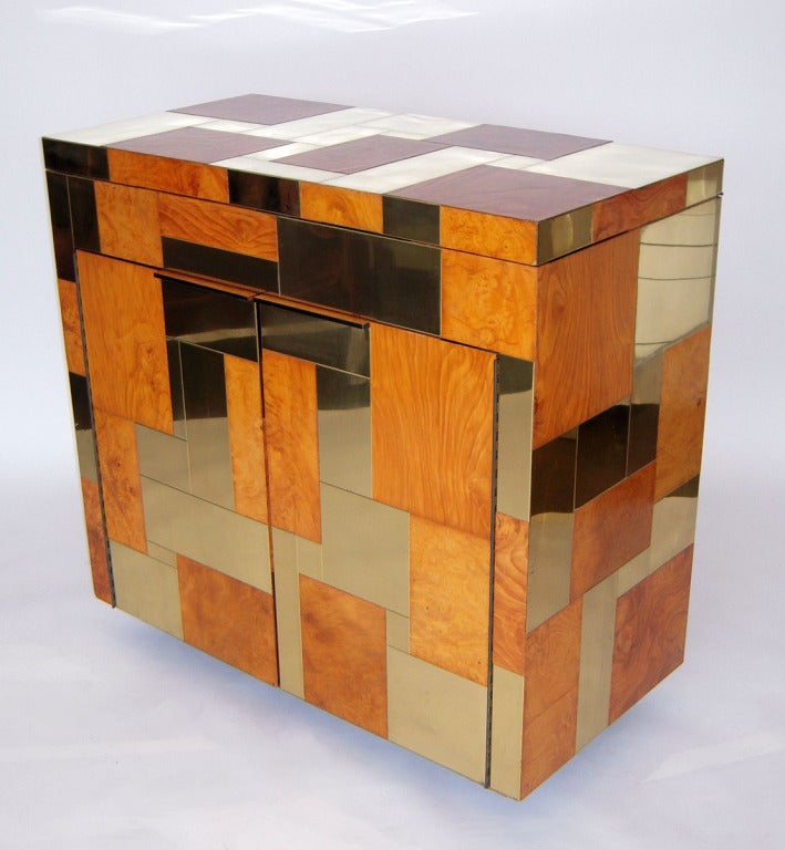 Cityscape brass and burled wood patchwork veneer cover this unique rolling bar cabinet. Double front doors reveal black interior with shelving, and the flip top props open to reveal a black lacquer holding compartment. On wheels.  Signed. This piece