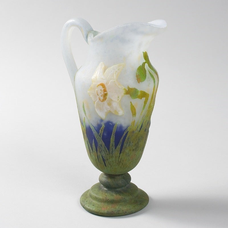 A French Art Nouveau wheel-carved cameo glass pitcher by Daum, featuring an applied flowering white jonquils with yellow centers, flower buds and blades of grass against a mottled blue and white ground, circa 1910.

Signed, “Daum Nancy” with the