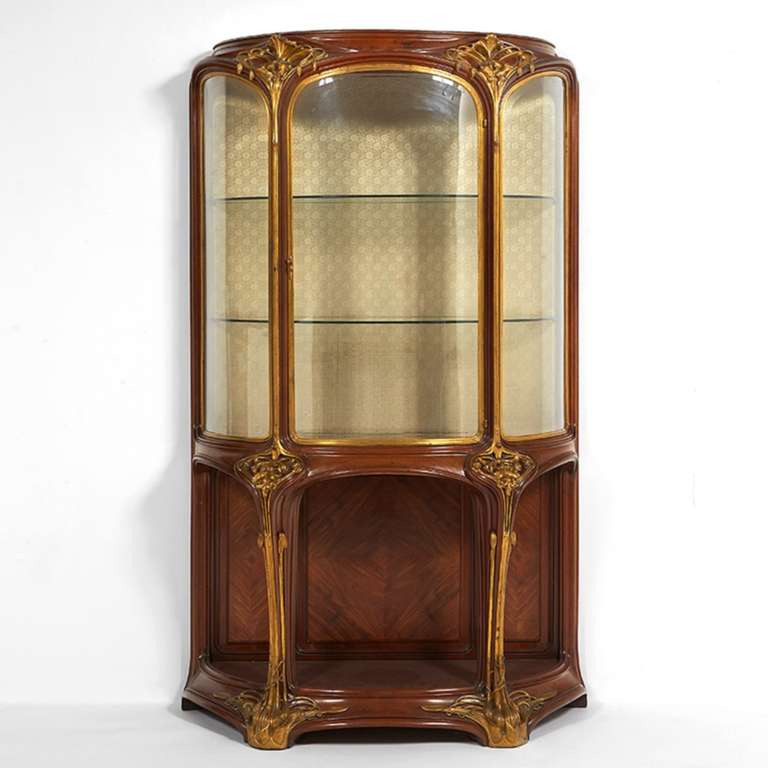 A French Art Nouveau carved mahogany and gilt-bronze bombé vitrine “Aux Orchidées” with original fabric upholstery by Louis Majorelle. The Orchid was part of the local flora in the Lorraine province and Majorelle spent many hours researching exotic