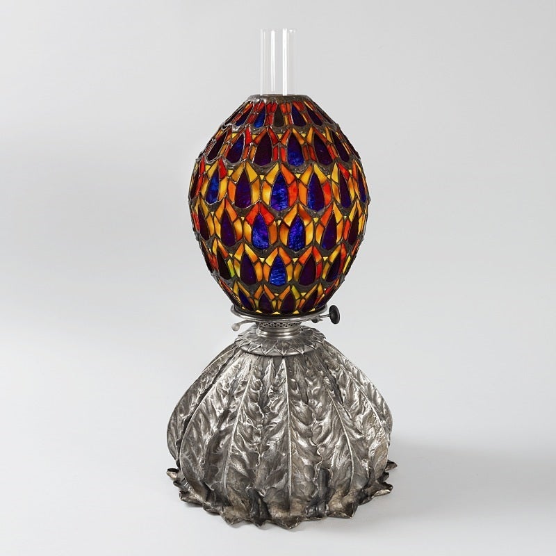 A Tiffany Studios New York converted “Oil Lamp,” with a repeat pattern of unfurled tobacco leaves on a silver brass base. 
Louis Comfort Tiffany’s fascination with the exotic is perhaps best seen in this very unusual converted oil lamp with a