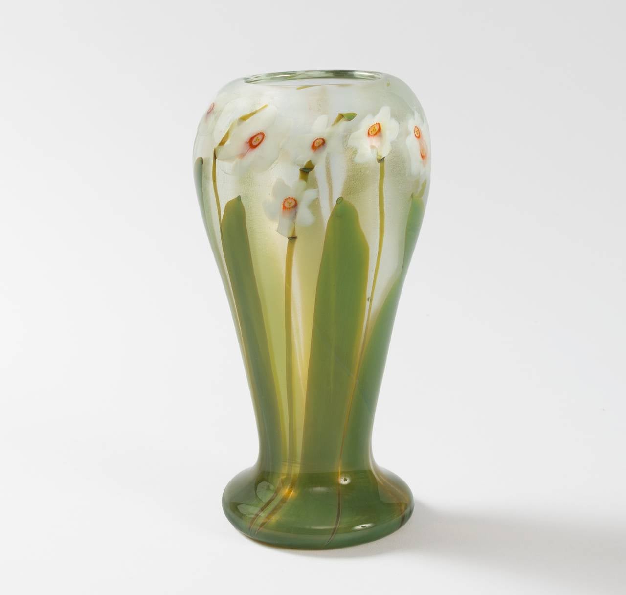 A Tiffany Studios New York Art Nouveau ‘paperweight’ glass vase. White blossoms with pink millefiori florets sprinkled throughout a green pulled-leaf motif, all featured on a clear background.

The paperweight technique involved fusing thin rods of