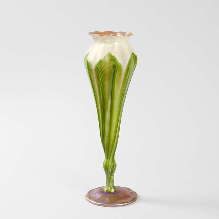 This Tiffany Studios New York flower form Favrile glass vase is uniquely shaped roughly in the silhouette of a curled flower not yet in bloom, with a rounded, rippled rim. The vase features a green pulled-feather decoration on a cream ground, each
