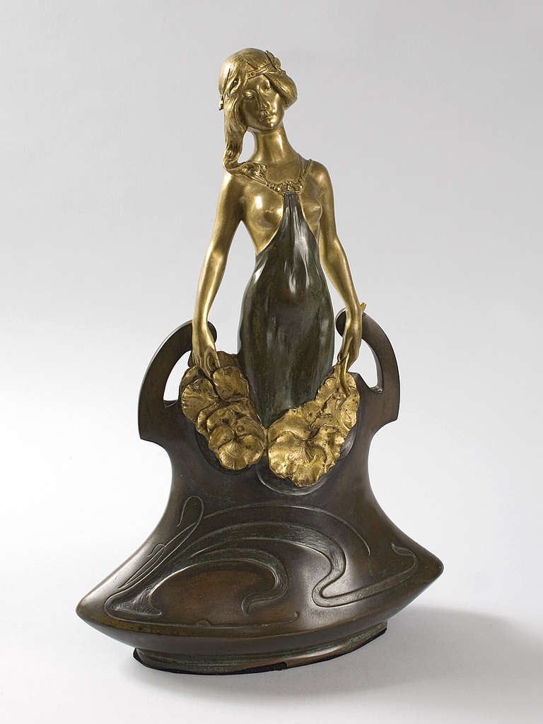 A French Art Nouveau bronze figural vase by Charles Korschann depicting a gilt maiden holding large flowers rising from a patinated bronze vase. Titled 