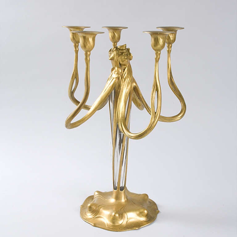 A German Art Nouveau gilt patinated pewter candelabra with a crystal center by Orivit of Cologne, depicting a woman decorated with flowers.  Her long hair is divided into 5 swirling tresses, each of which forms an individual candle holder.  With its